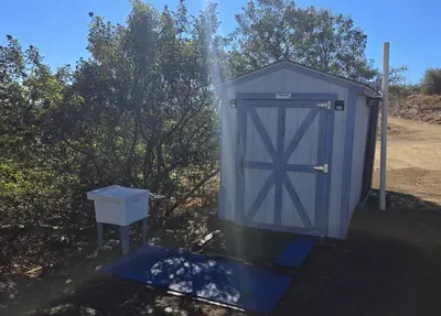a blue outhouse with a door next to some trees at A Quiet Fireside Retreat in a Scenic Glamping Dome in Fallbrook