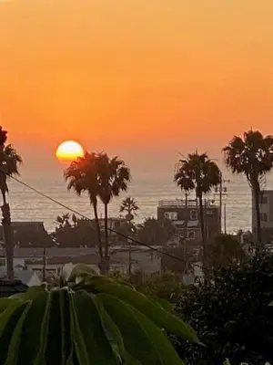 a sunset over a beach with palm trees and the ocean at Coral Cottage in San Diego