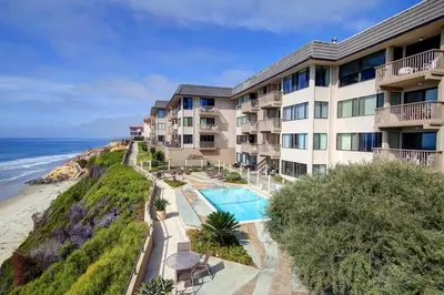 an apartment building with a swimming pool next to the ocean at Seaside Shenanigans - DMBC751P in Solana Beach