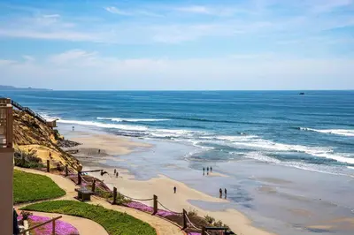 a beach with people walking on the sand and the ocean at A Wave From It All - SUR42 in Solana Beach