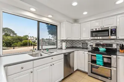 a kitchen with white cabinets and a large window at Drift Away - DMBC884 in Solana Beach