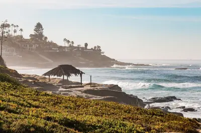 a beach with a straw umbrella and the ocean at Beachside 1BR Haven Near Ocean & Outdoor Space in San Diego