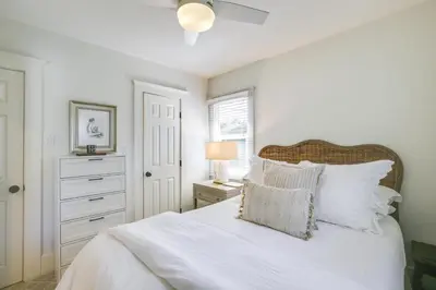a white bedroom with a bed with white sheets and pillows at Walkable Cottage Near Balboa Park with Yard and Grill! in San Diego