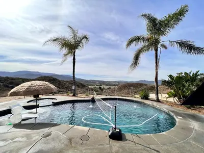 a swimming pool with palm trees and an umbrella at Temecula Wine Country Villa in Temecula