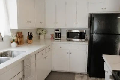 a kitchen with white cabinets and a black refrigerator at Designer Bungalow Steps to Beach in San Diego
