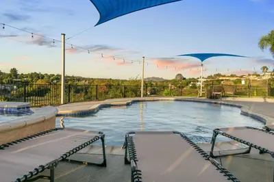 a large swimming pool with two benches and an umbrella at Sunset Crest - Home with stunning views, Pool, BBQ in Fallbrook