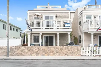 a large white house with a balcony on a street at Family-Friendly 3Br Steps From Beach - Walk To Everything By Beachview Rentals in Newport Beach