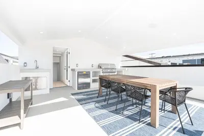 a white kitchen with a wooden table and chairs at Luxury 3Br W Rooftop Deck, Grill, Ac, Steps From The Sand By Beachview Rentals in Newport Beach