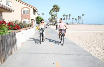 two people riding bikes down a sidewalk on the beach at Spacious 6Br W Oceanview And Garden Patio, Steps To Sand By Beachview Rentals in Newport Beach