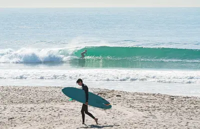 a person walking on the beach with a surfboard at 2Br Beach Escape W Oceanview Deck, 2 Houses From The Sand By Beachview Rentals in Newport Beach