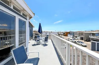 a balcony with chairs and an umbrella and the ocean at 2Br Beach Escape W Oceanview Deck, 2 Houses From The Sand By Beachview Rentals in Newport Beach