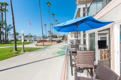 a table with a blue umbrella and chairs on a sidewalk at 3Br Oceanfront At Balboa Pier, Ac, Walk To It All By Beachview Rentals in Newport Beach