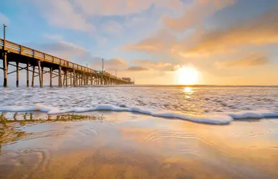 a pier on the beach with the sun setting at 6Br Oceanfront Duplex, Ac, Steps To Beach And Balboa Pier By Beachview Rentals in Newport Beach