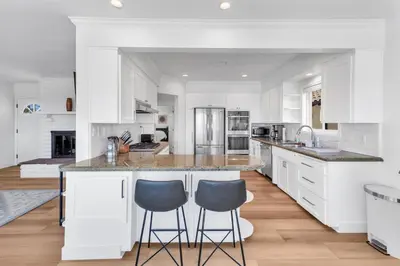 a kitchen with white cabinets and a large island with two bar stools at Stunning 3BR Capo Beach Home with Ocean Views in Dana Point