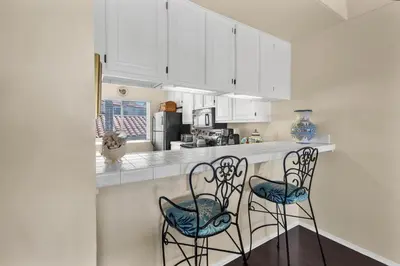 a kitchen with white cabinets and two chairs at a counter at 2BR Condo with Views Near Shops and Food, Fast WiFi in Carlsbad