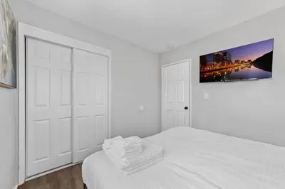 a white bedroom with a bed and a tv on the wall at Charming Gem in LH, High Speed WiFi Minutes from Beach, Downtown & Petco Park! in San Diego