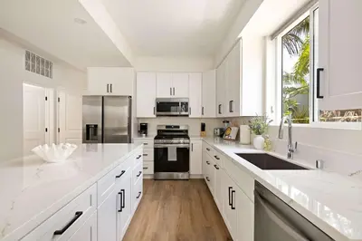 a white kitchen with white cabinets and a large window at Ocean Beach Getaway with Peek Views in San Diego