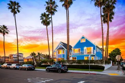 a blue house with palm trees in a parking lot at OB Cottage Beach Views in San Diego