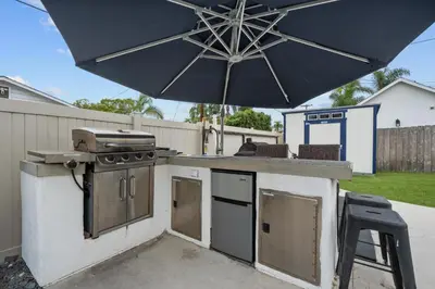 an outdoor kitchen with a grill and an umbrella at Cozy Room with Hot Tub, Pool, Sauna & Gym Near Beach in Oceanside