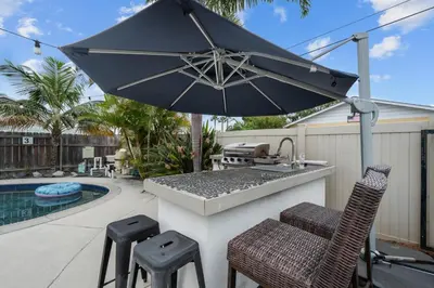 a outdoor kitchen with an umbrella and stools at Cozy Room with Hot Tub, Pool, Sauna & Gym Near Beach in Oceanside