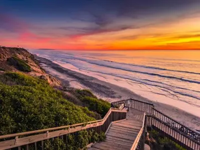 a staircase leading to the beach with a sunset at Oceanview Oasis with Roofdeck Hot Tub in Carlsbad