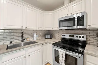 a kitchen with white cabinets and a stove and a microwave at Historic Apartment with Roof Deck in the Heart of North Park in San Diego