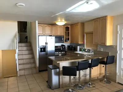 a kitchen with a refrigerator and a counter with stools at Ocean Front On Beach! -2 Master BR, 2 Full BA, Patio!, AC, Parking, Close to All in San Diego