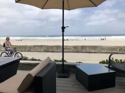 a woman riding a bike next to a beach with an umbrella at Ocean Front Beauty right on Best Beach in Mission Beach, San Diego! in San Diego