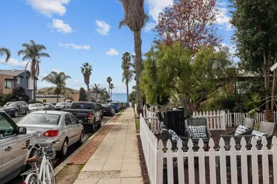 a white fence next to a street with parked cars at Ocean Paradise | Patio, Parking, BBQ, Location! in San Diego