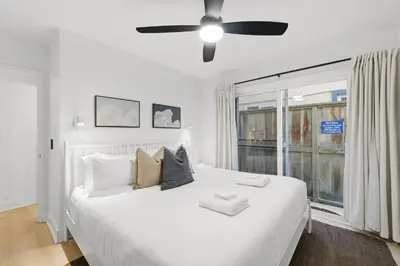 a bedroom with a white bed with a ceiling fan at Bayfront Getaway | 2BR Retreat w/ Patio & BBQ, Steps to Sand in San Diego