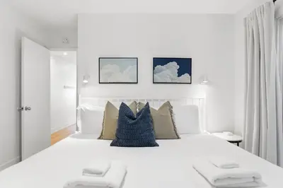 a white bedroom with a large white bed with pillows at Bayfront Getaway | 2BR Retreat w/ Patio & BBQ, Steps to Sand in San Diego