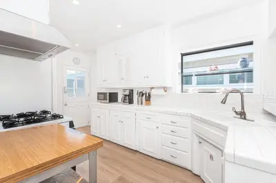 a white kitchen with white cabinets and a sink at Bayfront 3Br With Harbor Views, Only Steps To The Beach By Beachview Rentals in Newport Beach