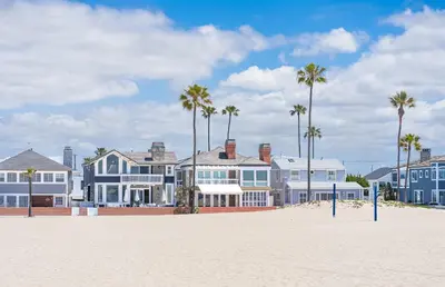 a row of houses on the beach with palm trees at Bayfront 3Br With Harbor Views, Only Steps To The Beach By Beachview Rentals in Newport Beach
