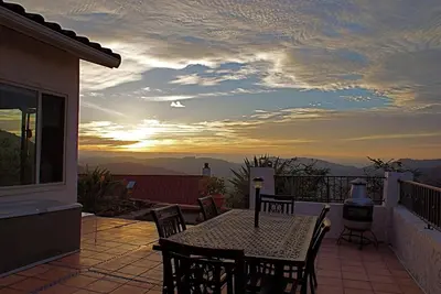 a table and chairs on a balcony with a sunset at Quiet Hilltop Home With Stunning Hill Top And Valley Views in Valley Center