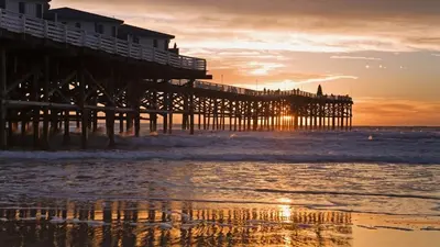 a pier on the beach at sunset with the ocean at The Seabreeze by Coastline Vacation Rentals in San Diego