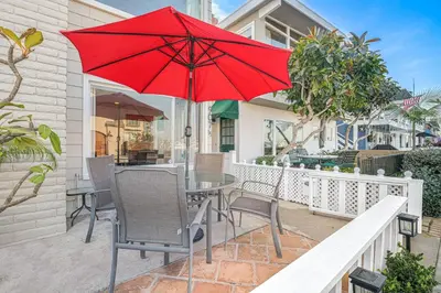 a patio with a table and chairs and a red umbrella at Bayfront 2Br With Harbor Views, Only Steps To The Sand By Beachview Rentals in Newport Beach