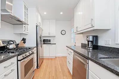 a kitchen with white cabinets and a wooden floor at Bayfront 2Br With Harbor Views, Only Steps To The Sand By Beachview Rentals in Newport Beach
