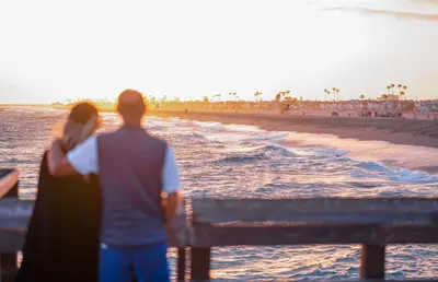 a man and a woman standing on a bench near the beach at Bayfront 2Br With Harbor Views, Only Steps To The Sand By Beachview Rentals in Newport Beach