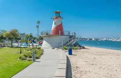 a red and white lighthouse next to a beach at Bayfront 2Br With Harbor Views, Only Steps To The Sand By Beachview Rentals in Newport Beach