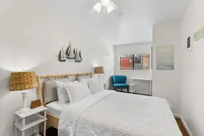 a white bedroom with a bed and a blue chair at The Sands by Coastline Vacation Rentals in San Diego