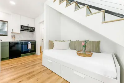 a white living room with a couch under the stairs at PB Beach Compound - 2 New Homes Steps to Sand in San Diego