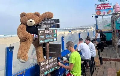 a teddy bear sitting on a sign at the beach at ITH San Diego Beach Bungalow Surf Hostel in San Diego