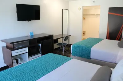 a hotel room with two beds and a desk with a television at Howard Johnson by Wyndham San Diego Hotel Circle in San Diego