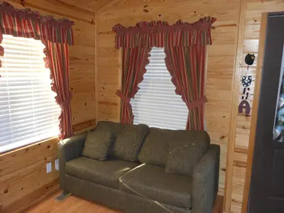 a living room with a couch in front of two windows at Oakzanita Springs Camping Resort Cabin 2 in Descanso