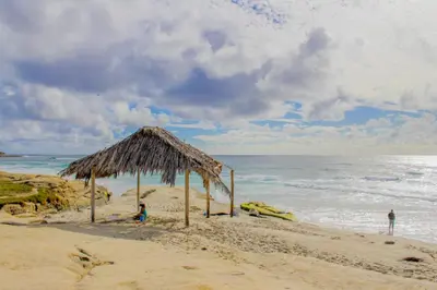 a straw hut on a sandy beach next to the ocean at La Jolla Cottage in San Diego