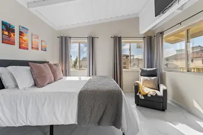 a bedroom with a bed and a chair and windows at Sweet Sunset Studio in San Diego