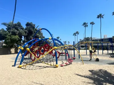a child playing on a playground in the sand at Sweet Beach Duplex in Newport Beach