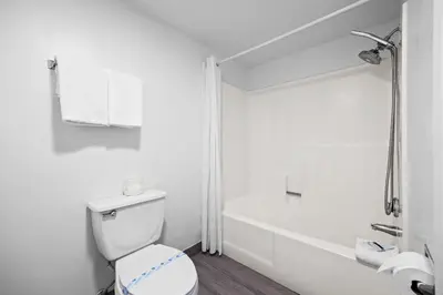 a white bathroom with a toilet and a bath tub at Hotel Milagro in Chula Vista