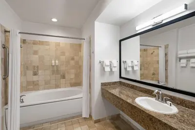 a bathroom with a sink and a tub and a mirror at Ramada Suites by Wyndham San Diego Hotel Circle Area in San Diego