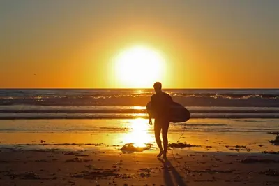 a man walking on the beach at sunset with a surfboard at Courtyard by Marriott San Diego Downtown Little Italy in San Diego